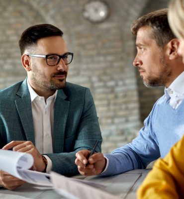 Insurance agent having a meeting with a couple and offering them to sign an agreement in the office.